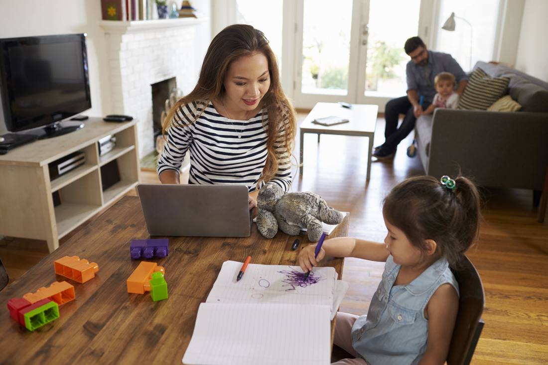 A family sitting together at a kitchen table looking at a laptop.